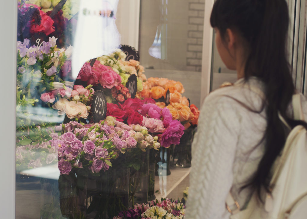 Girl looks at the flower shop window with different varieties of roses.