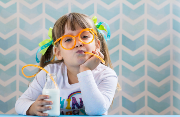 Sweet girl kid drinking milk with funny glasses straw. Growing up concept