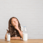 Young hispanic kid sitting on the table drinking a glass of milk serious face