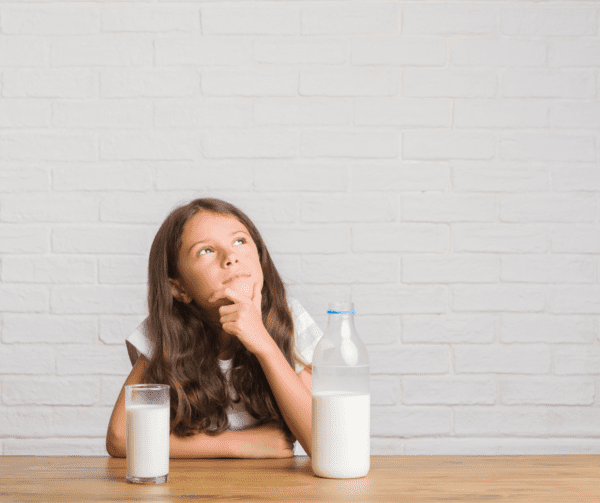 Young hispanic kid sitting on the table drinking a glass of milk serious face